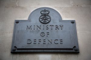 Plaque on a stone wall reading 'Ministry of Defence' with a crown and military emblem above the text.