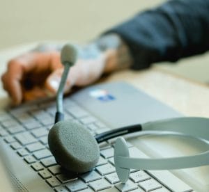 Close-up of a headset resting on a laptop keyboard with a tattooed hand typing in the background.